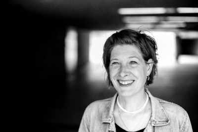 Auf dem schwarz-weiß Portrait sieht man eine weiße weiblich gelesene Person lachen.